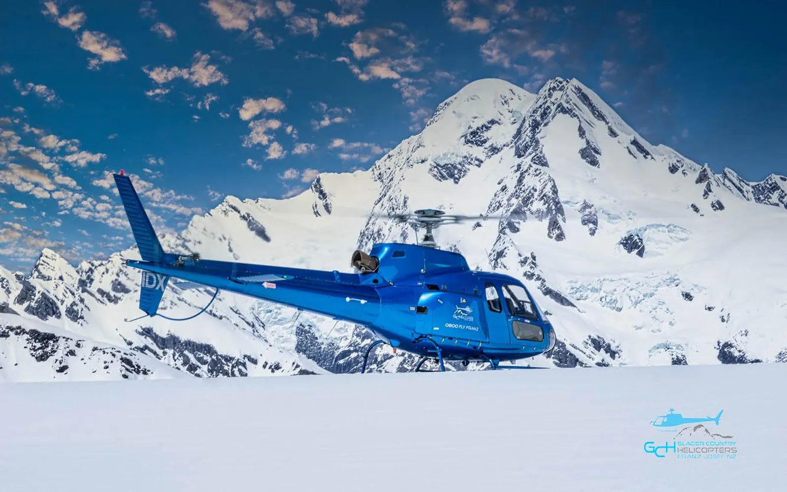 A helicopter on the snowfield above Franz Josef Glacier with the peaks of the Southern Alps behind