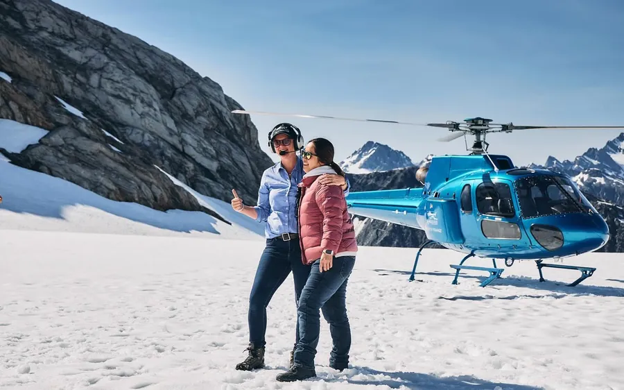Two walkers sitting on the snow beside a helicopter