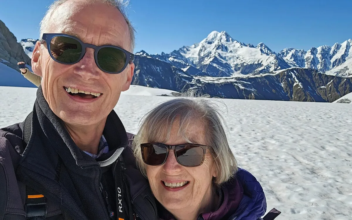 Two passengers on the snow with the Southern Alps behind them